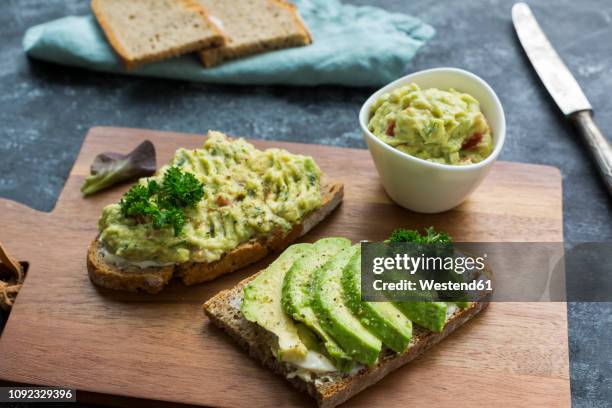 slices of bread with sliced avocado and avocado cream on wooden board - avocado stock-fotos und bilder