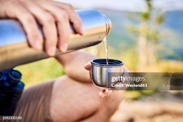 close-up of man during hiking trip pouring cold water from thermos flask - drinks flask stock pictures, royalty-free photos & images