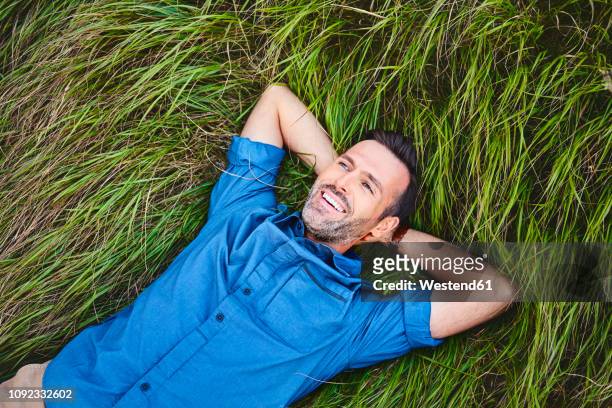 relaxed happy man lying in grass - hände hinter dem kopf stock-fotos und bilder