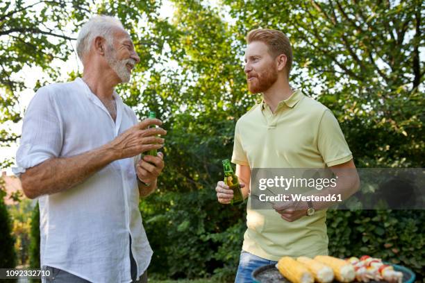 senior father and adult son having a barbecue and talking in garden - party host stock-fotos und bilder