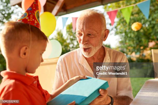grandfather handing over present to grandson on a garden birthday party - gift lounge stock-fotos und bilder