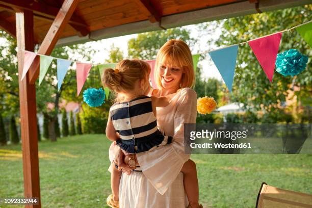 happy mother carrying her daughter on a garden birthday party - birthday streamers stock-fotos und bilder