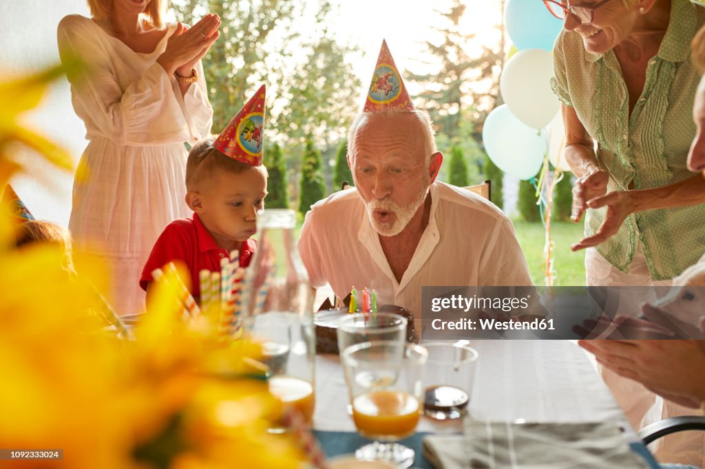 Happy extended family blowing out candles on birthday cake on a garden party