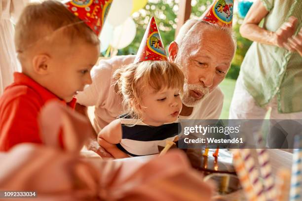 grandfather and grandchildren blowing out candles on birthday cake on a garden party - birthday stock-fotos und bilder