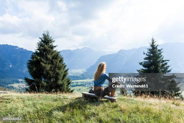 germany, bavaria, oberammergau, young woman hiking sitting on bench on mountain meadow - oberammergau stock pictures, royalty-free photos & images