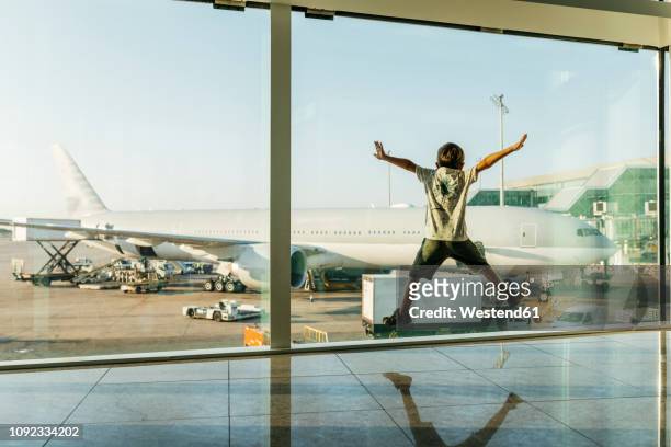 spain, barcelona airport, boy in departure area, jumping in front of glass pane - kid in airport stock-fotos und bilder