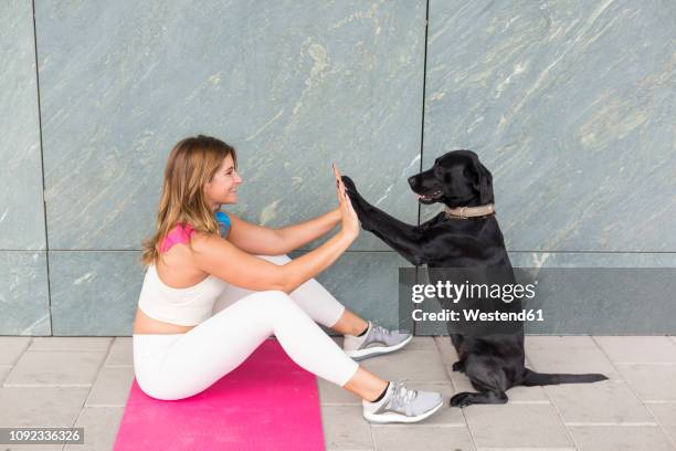 young woman sitting on yoga mat doing relaxation exercise with her black dog - dog yoga stock pictures, royalty-free photos & images