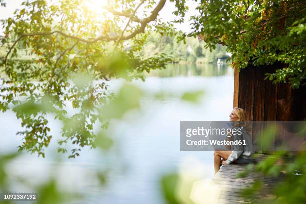 relaxed woman sitting on wooden jetty at a remote lake - paso entablado fotografías e imágenes de stock