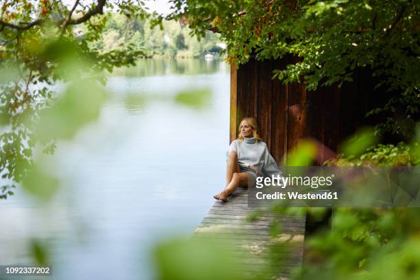 relaxed woman sitting on wooden jetty at a remote lake - holzsteg stock-fotos und bilder
