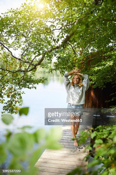 smiling woman standing on wooden jetty at a remote lake - older woman legs fotografías e imágenes de stock