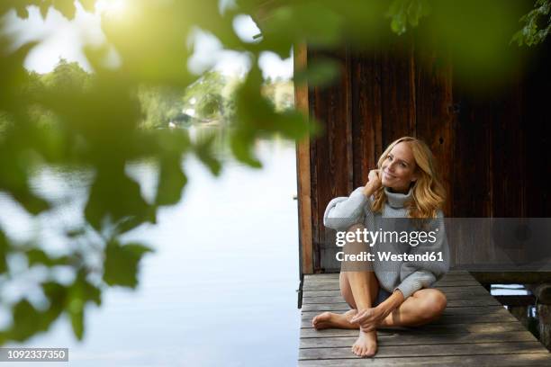 smiling relaxed woman sitting on wooden jetty at a remote lake - long jetty stock pictures, royalty-free photos & images