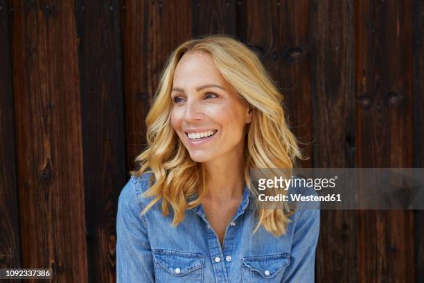 happy blond woman in front of wooden wall - capelli biondi foto e immagini stock