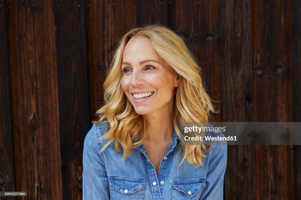 Happy blond woman in front of wooden wall