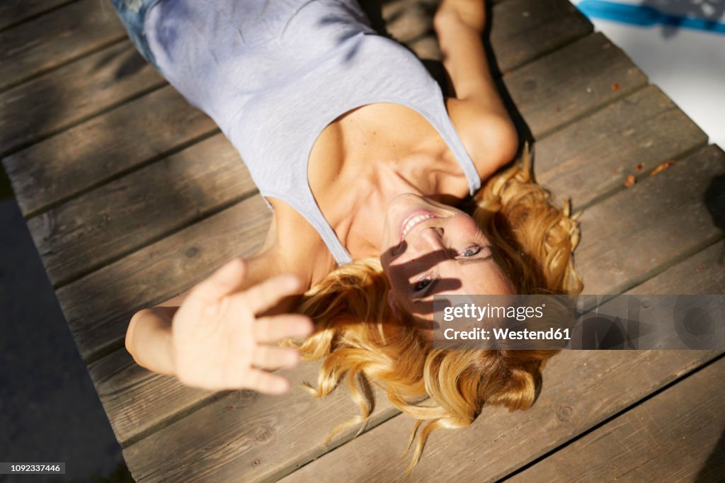 Happy blond woman lying on wooden jetty in sunshine