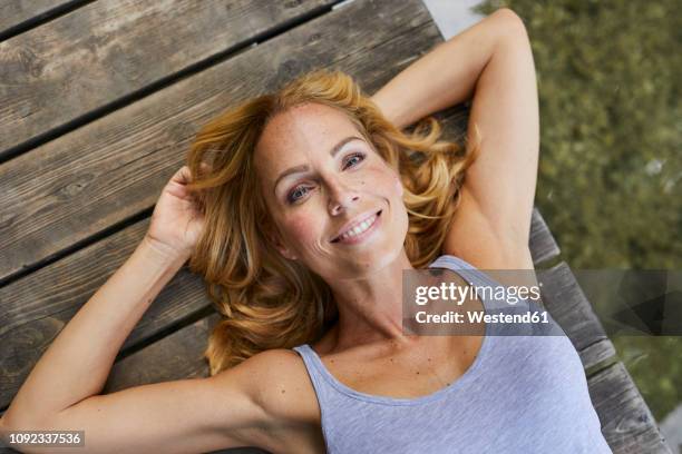 portrait of smiling blond woman lying on wooden jetty at a lake - boardwalk stock-fotos und bilder