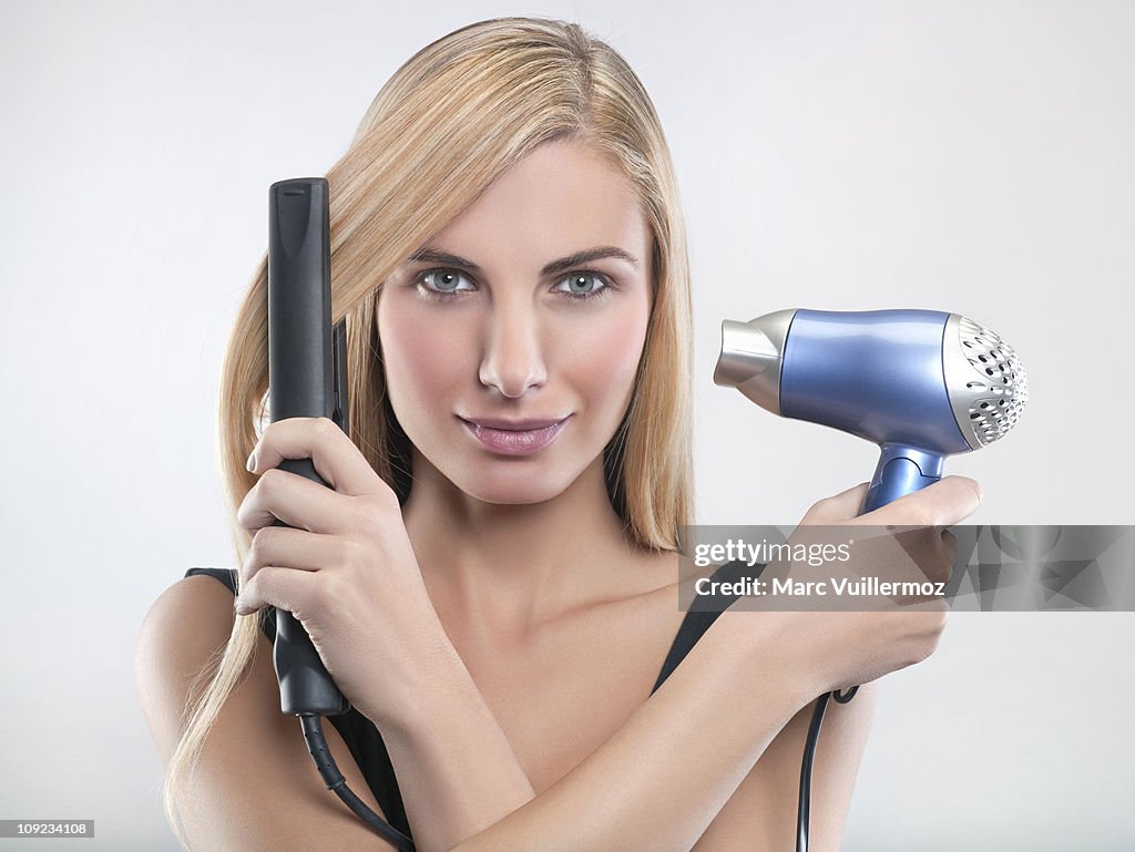 Young woman using hair straighteners and hair dryer