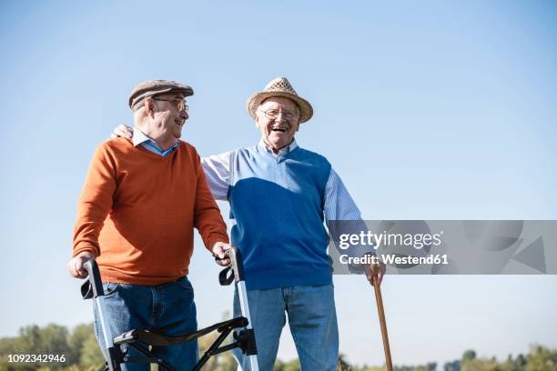 old friends taking a stroll in the fields with walking stick and wheeled walker, talking about old times - mobility walker stock-fotos und bilder