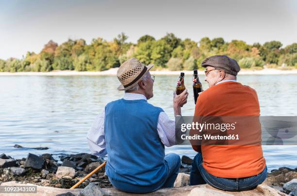 old friends sitting by the riverside, drinking beer - senior men beer stock pictures, royalty-free photos & images