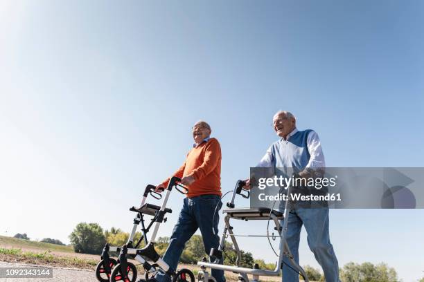 two old friends walking on a country road, using wheeled walkers - rollator stock-fotos und bilder