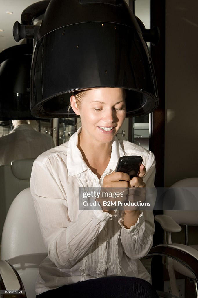 Woman using phone under hairdryer