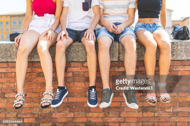 legs of friends sitting together on a wall - teen boy shorts stock-fotos und bilder