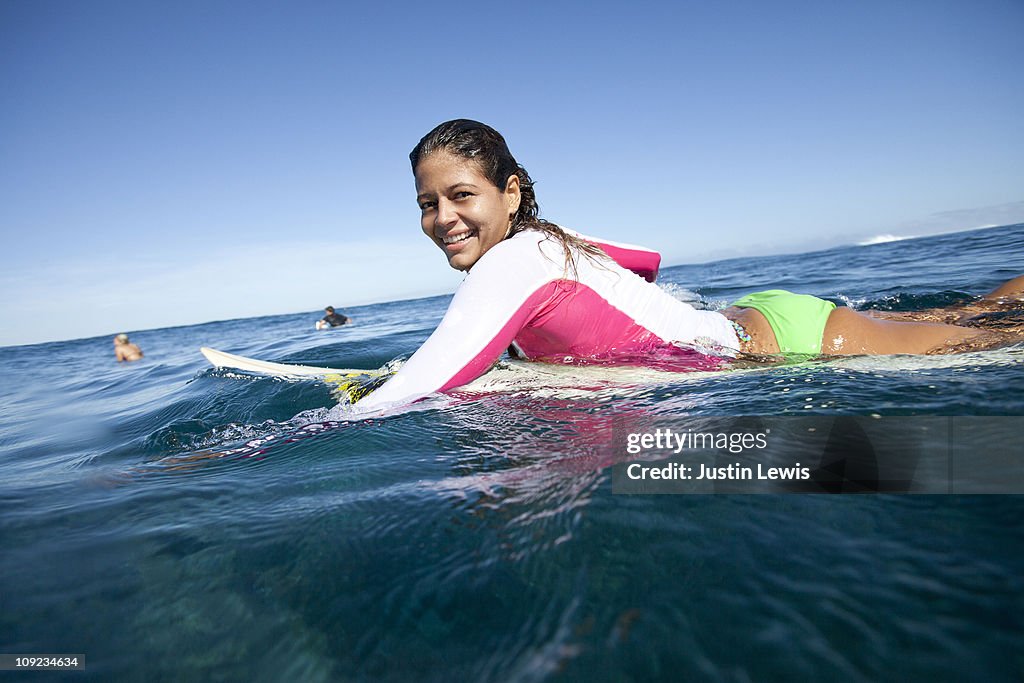 Female surfer paddling in clear water.