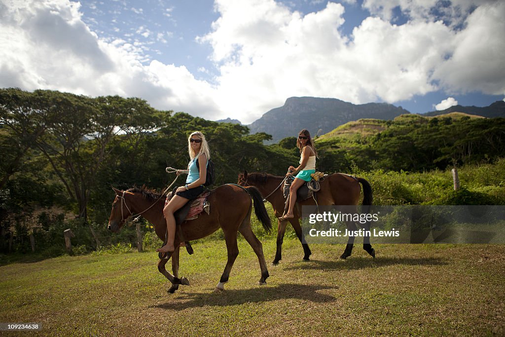 Two girls ridding horses in the tropics.