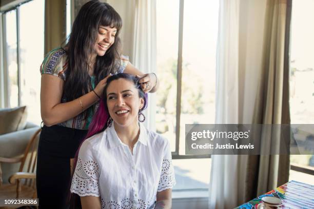 millennial latina girlfriends getting ready for a party, one is braiding the other's hair, both smiling, indoors - one friend helping two other imagens e fotografias de stock