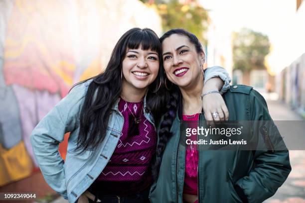 two young latina women leaning together, smiling and happy - gray coat stock pictures, royalty-free photos & images
