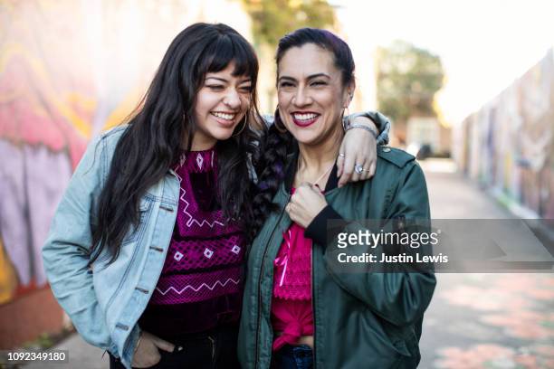 two latina friends laughing while standing in mural alley in san francisco's mission district - friends women makeup stockfoto's en -beelden
