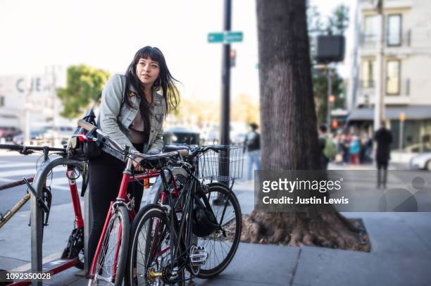 millennial latina bicycle commuting, locking her bike on city sidewalk - hauptverkehrszeit stock-fotos und bilder