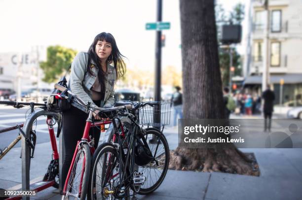 millennial latina bicycle commuting, locking her bike on city sidewalk - commuter cyclist stock pictures, royalty-free photos & images