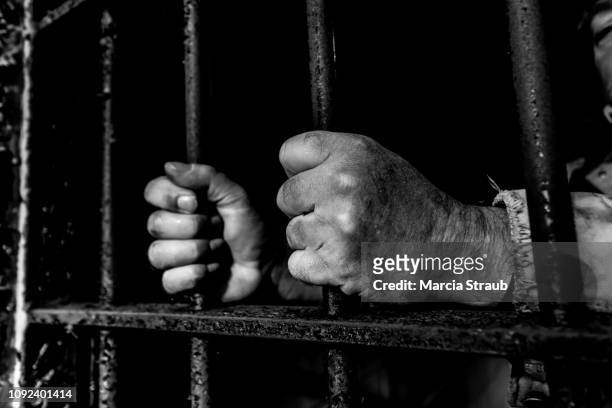 prisoner's hands on outdated, old, prison cell door - old prisoner stock pictures, royalty-free photos & images