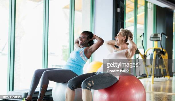 two women at the gym on medicine balls, talking - women working out gym stock pictures, royalty-free photos & images
