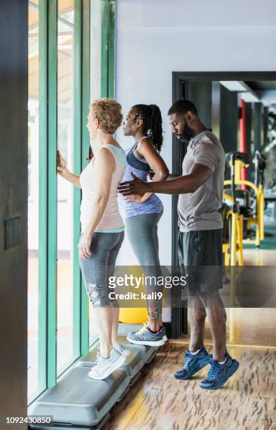 dos mujeres con entrenador personal en gimnasio, becerro plantea - female muscular calves fotografías e imágenes de stock