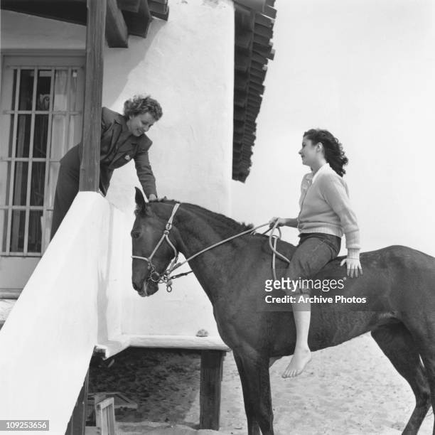 British-born actress Elizabeth Taylor on horseback on a beach with her mother Sara, circa 1949.