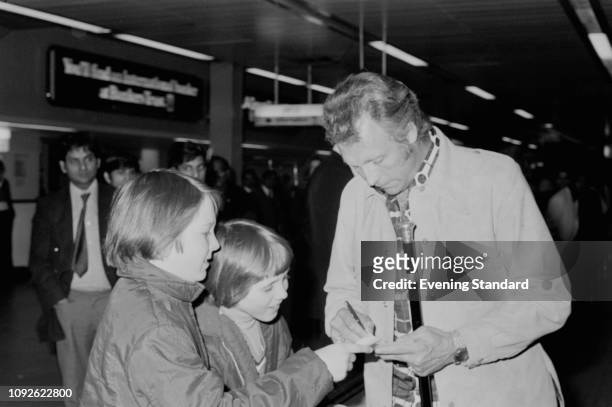 American stunt performer and entertainer Evel Knievel signing autographs to two boys while at the airport, UK, 9th May 1975.