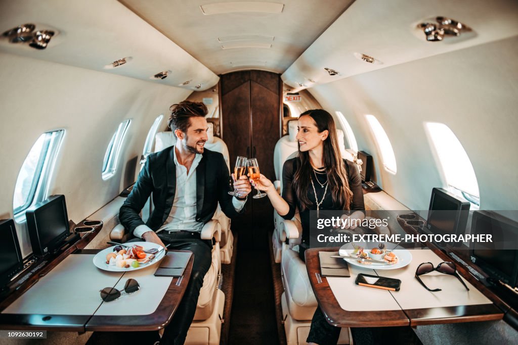 Succesvolle paar maken een toast met champagne glazen terwijl het hebben van canapeetjes aan boord van een prive vliegtuig