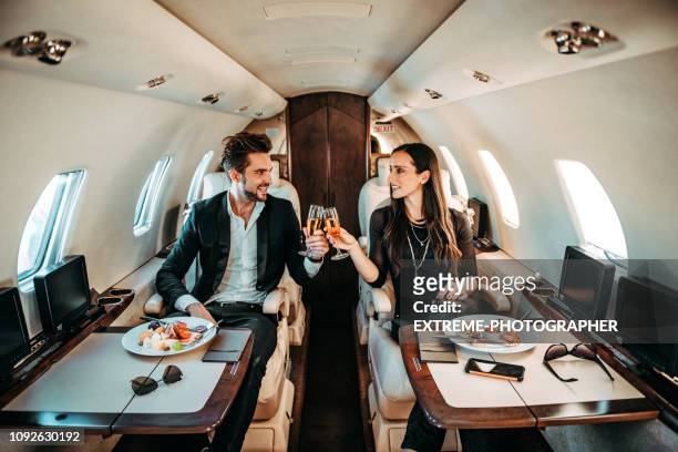succesvolle paar maken een toast met champagne glazen terwijl het hebben van canapeetjes aan boord van een prive vliegtuig - couple airplane stockfoto's en -beelden