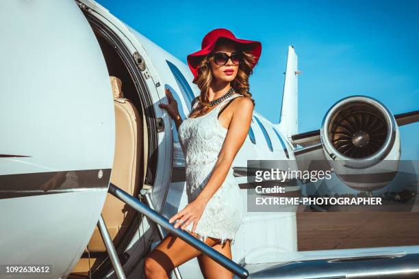 beautiful female fashion model entering a private jet parked on a taxiway - billionaires stock pictures, royalty-free photos & images