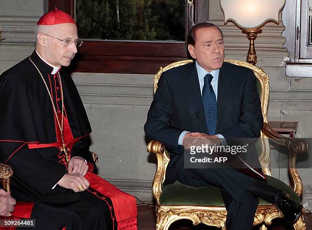 Italian Premier Silvio Berlusconi grimaces next to Cardinal Angelo Bagnasco at the Italian Embassy to the Holy See in Rome on February 18 during...