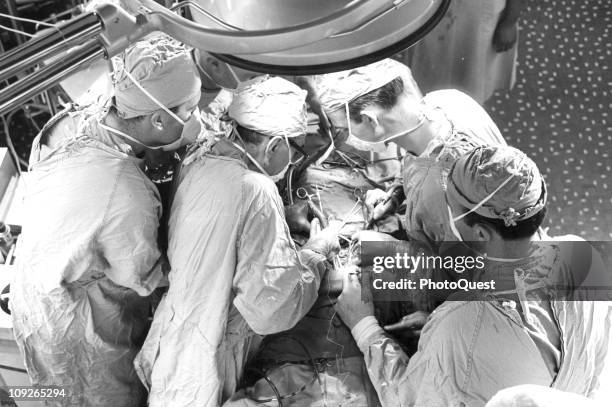 Doctor Michael DeBakey, wearing horn-rimmed glasses, completes replacement of a patient's defective aortic valve with an artificial valve, Houston,...