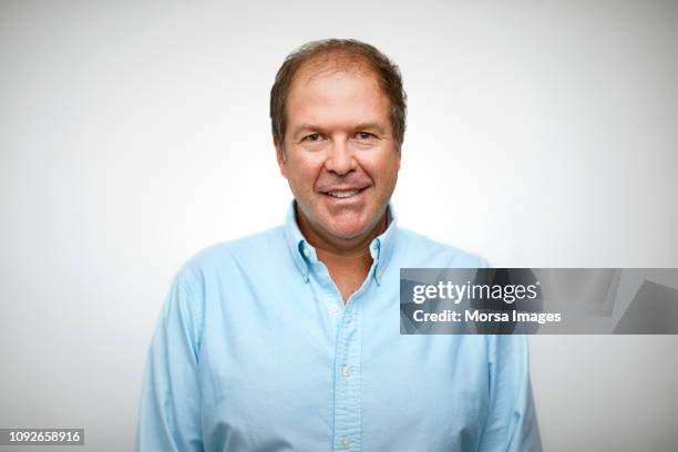 portrait of senior man smiling against white - blauw shirt stockfoto's en -beelden