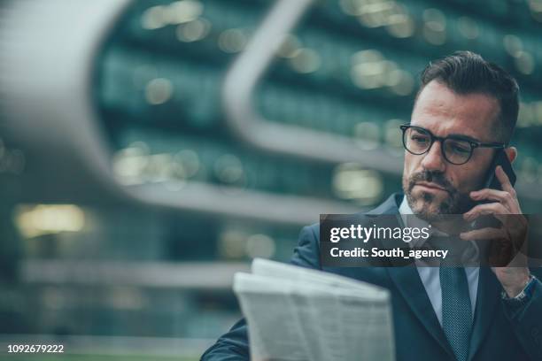 gentleman reading newspaper and talking on mobile - business people and paper imagens e fotografias de stock