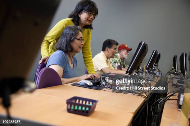 teacher helping students on computers in computer lab - avondschool stockfoto's en -beelden