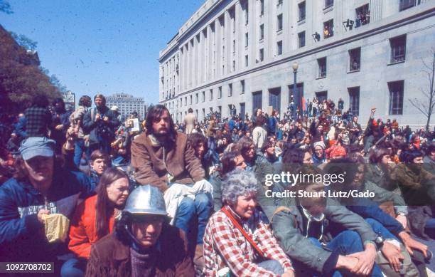 During the 1971 May Day Protests against the Vietnam War, a large number of warmly dressed male and female protestors sit together, on a sunny day,...