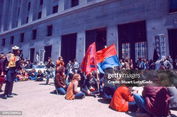 During the 1971 May Day Protests against the Vietnam War, a large circle of warmly dressed male and female protestors sit together outside the US...