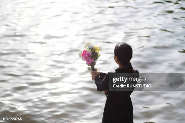 bereaved holding flowers against river - funeral grief flowers stock-fotos und bilder