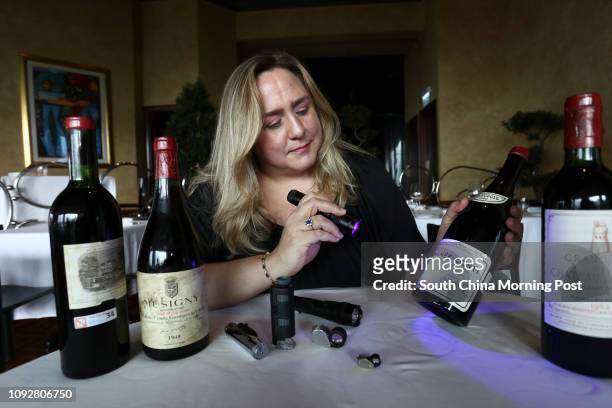 Maureen Downey, fake wine expert, uses a blue light to check the capsule, and cork, and used to see the age of the paper used in the label, on a...