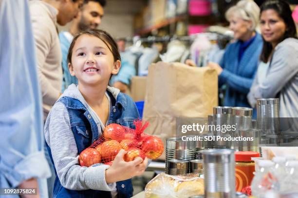 smiling little girl donates apples to food bank - banco alimentar imagens e fotografias de stock